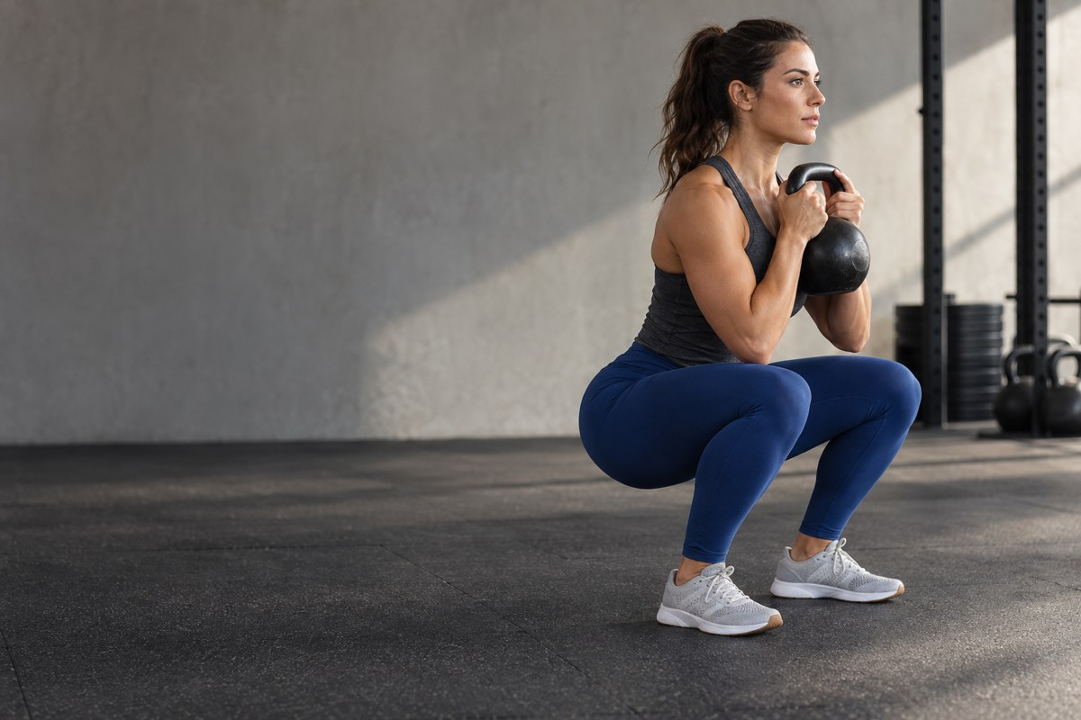 A woman practising a kettlebell squat in a bright gym